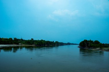 Nehir kıyısının manzarası, ağaçlar, dağ ve mavi gökyüzü
