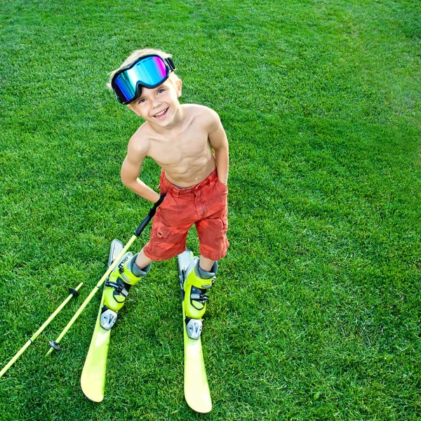 Funny little skier with ski on a green grass. Active helathy childhood concept