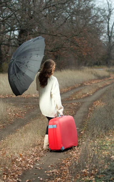 A woman with suitcase and unbrella in autumn scenery