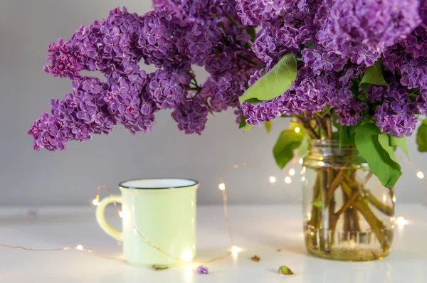 ライラックの花束のカップとお祭りのライト テーブルの上 — ストック写真