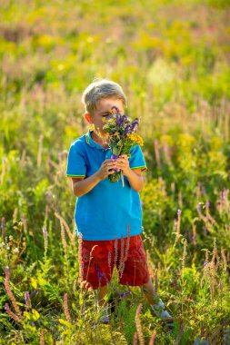 Yeşil doğal arka planda çiçekleri olan küçük çocuk.