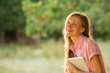 Elinde kitap tutan genç bir kadın, parkta bir masa.
