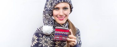 Noel kıyafetli neşeli genç bir kadın örgü şapka ve süveter giyip beyaz üzerine izole edilmiş sıcak bir içecek tutuyor.