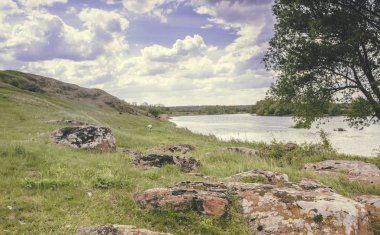 Güney Böcek Nehri 'nin kayalık kıyısı. Güneşli bir günde mavi gökyüzüne karşı yeşil çimenler ve kırmızı taşlar. Ukrayna