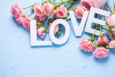 Kartpostal. Beyaz ahşap harfler ve pembe güller çiçek ışık mavi dokulu arka plan üzerinde yapılan kelime aşk.