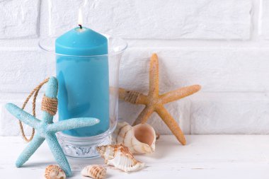 Yanan mum, kabukları ve deniz yıldızı yakınındaki beyaz tuğla duvar tarafından mavi. Seçici odak. Metin için yer.