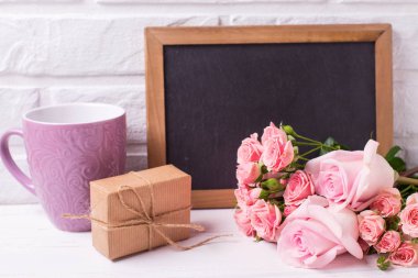 Pembe gül çiçek, boş yazı tahtası, mevcut ve menekşe Kupası Beyaz ahşap zemin üzerinde kutusuyla. Çiçekli natürmort. Seçici odak. Metin için yer.