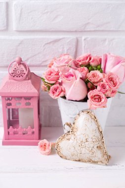 Pembe gül çiçek beyaz pot, dekoratif kalp ve pembe fener beyaz duvara karşı. Çiçekli natürmort. Seçici odak. Dikey görüntü.