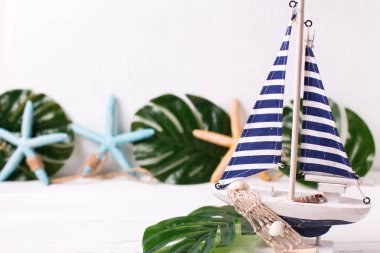Dekoratif ahşap oyuncak tekne, deniz yıldızı ve tropikal bitki yaprakları beyaz dokulu arka plan üzerinde. Metin için yer. Yaz, tatil kavramı