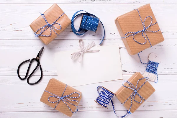Boş etiket ve hediyeleri, makas, mavi kurdele ve dokulu ahşap arka plan etiketleri ile sarılmış hediye kutuları. Seçici odak. Metin için yer. Düz yatıyordu