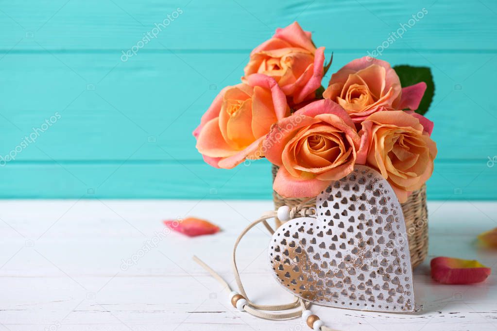 Decorative heart and  fresh roses flowers on white wooden background against  turquoise  wall. Place for text. Floral still life. Selective focus.
