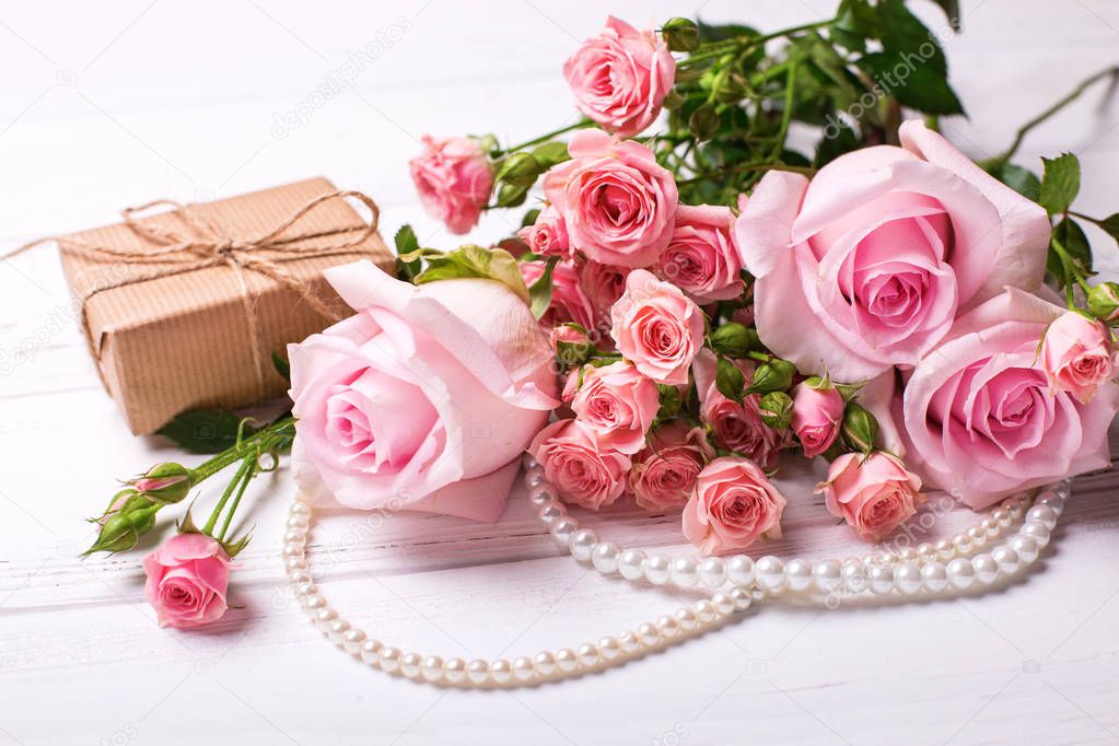 Fresh pink roses flowers  and  wrapped box with present on white wooden background. Floral still life.  Selective focus.