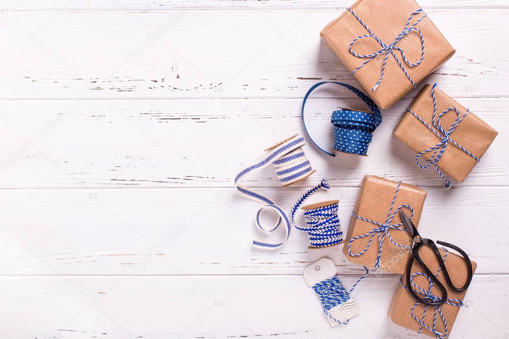 Wrapped  gift boxes with presents, scissors,  blue ribbon  and tags on textured wooden background. Selective focus. Place for text. Flat lay.