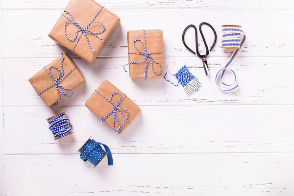 Праздничные подарочные коробки с подарками, ножницами, голубой лентой и бирками на текстурированном деревянном фоне. Выборочный фокус. Место для смс. Плоский лежал
.