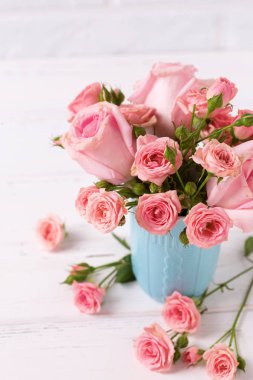 Pembe gül çiçek beyaz duvara karşı mavi Kupası. Çiçekli natürmort. Seçici odak. Dikey görüntü.