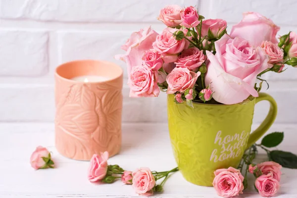 Pembe gül çiçek yeşil Kupası ve yanan mum beyaz duvara karşı. Çiçekli natürmort. Seçici odak. 
