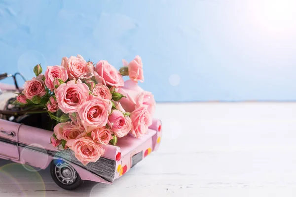 Retro car with pink roses flowers against blue wall. Romantic background. Selective focus. Place for text.