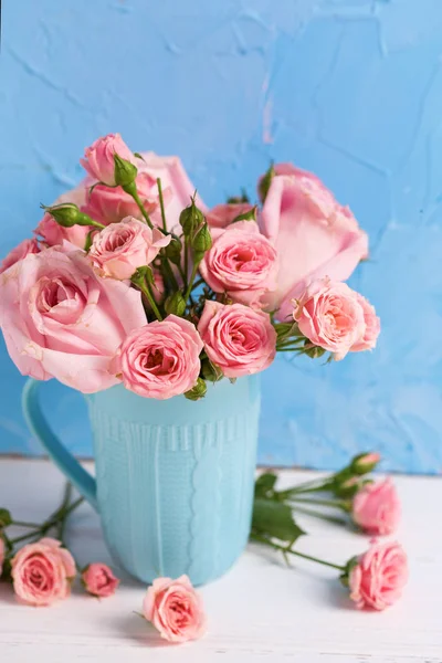 粉红色玫瑰花在蓝色杯子反对蓝色纹理墙壁 — 图库照片