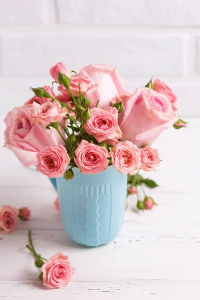 粉红色玫瑰花在蓝色杯子反对白色砖墙 — 图库照片