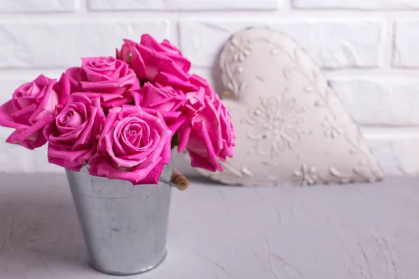 Bright pink roses flowers in bucket and heart on grey background against white wall