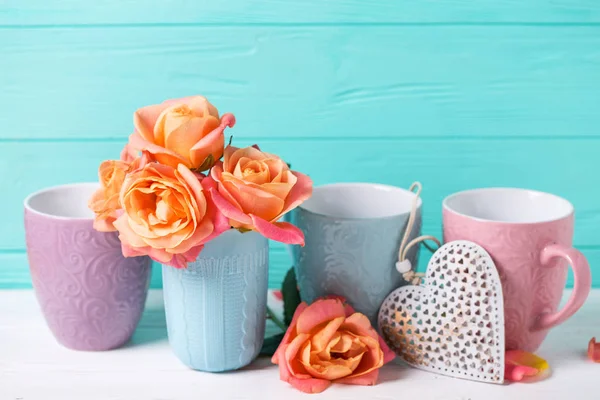 Bunch of fresh orange roses in cup and heart against turquoise wall