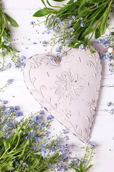 Big vintage heart and frame from blue forget-me-nots or myosotis flowers on white wooden background