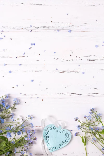 Border from blue forget-me-nots or myosotis flowers and heart on white wooden background