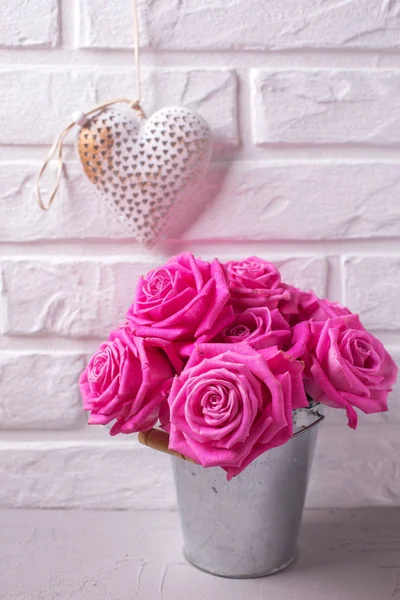 Bright pink roses flowers in bucket and heart on grey background against white wall