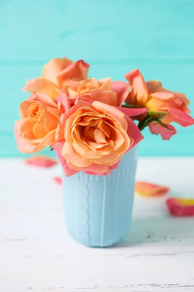 Fresh orange roses in blue cup on turquoise wall background