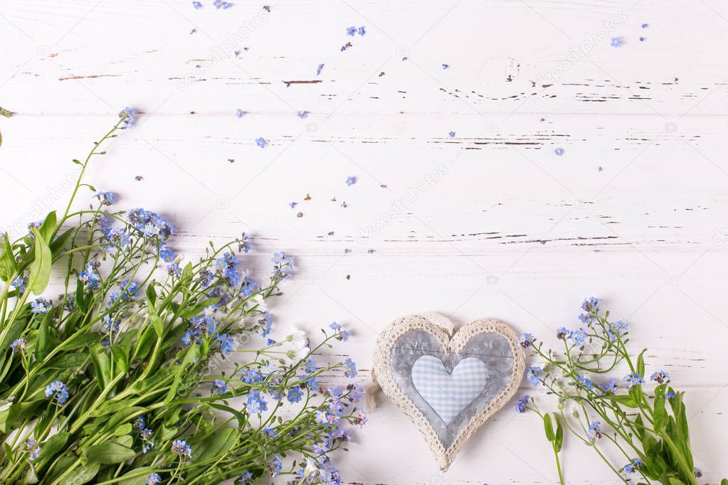 Frame from blue forget-me-nots or myosotis flowers and heart on white wooden background 