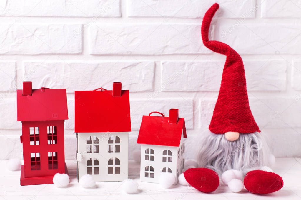 Decorative houses and elf or gnome on white wooden background against brick wall