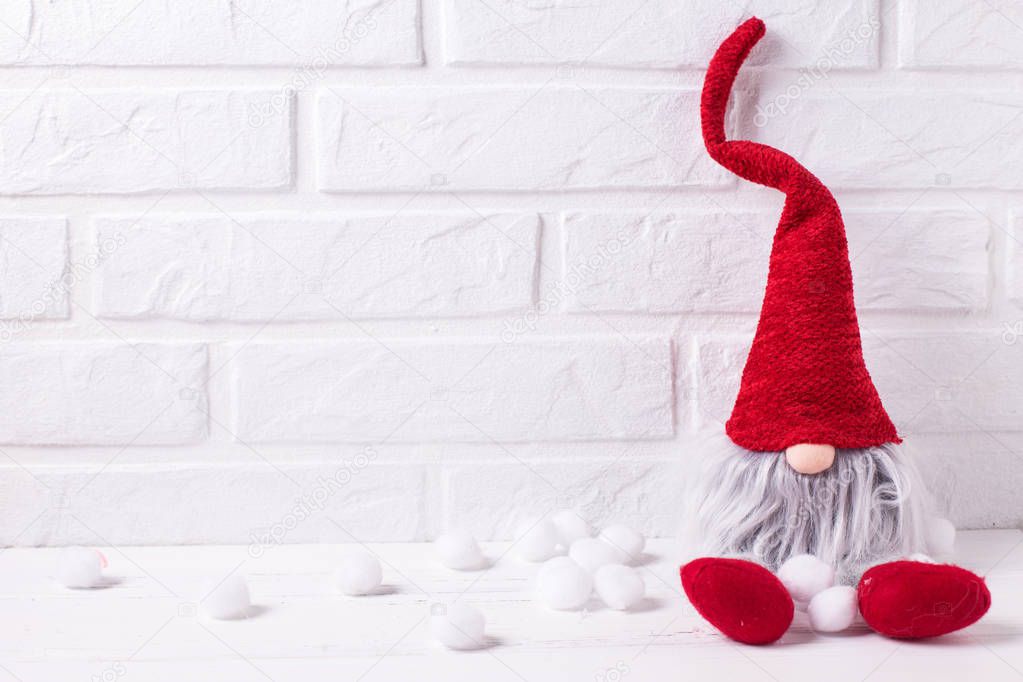 Decorative Christmas elf or gnome on white wooden background against brick wall