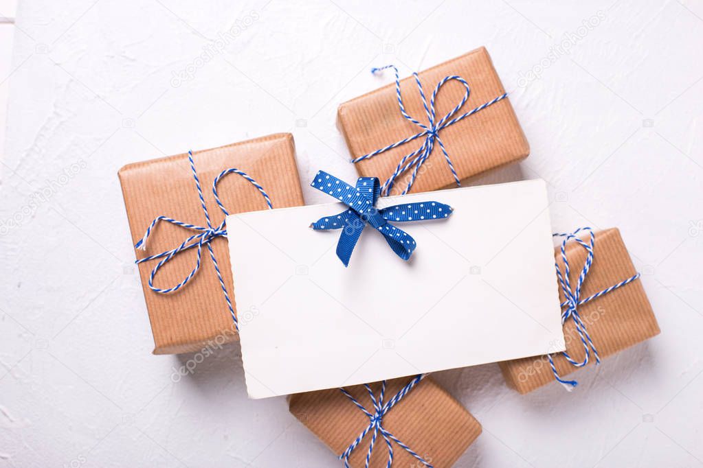 Empty tag and wrapped gift boxes with presents and blue ribbons on textured wooden background