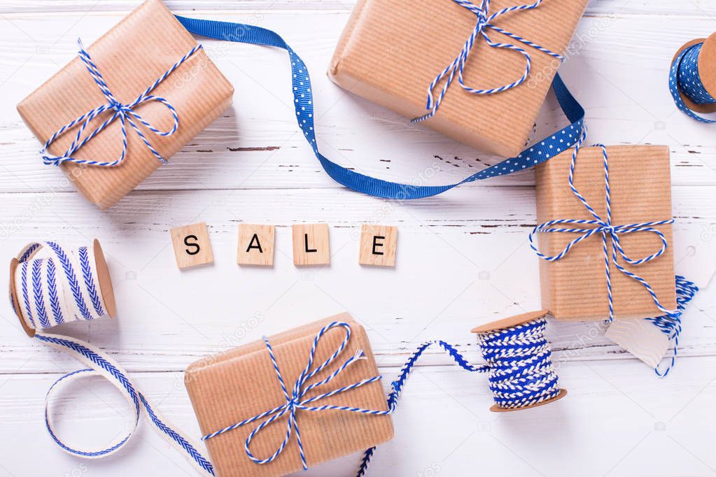 Word sale made from wooden blocks and gift boxes with presents, blue ribbons on textured wooden background