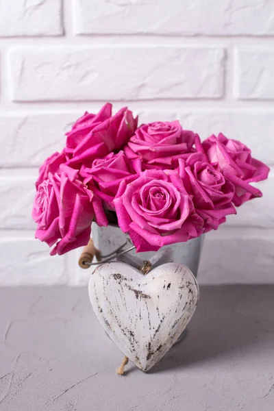 Bright pink roses flowers in bucket and heart on grey background