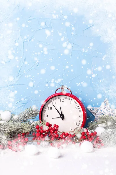 Holiday background. Clock,  berries and fir tree branches with bokeh lights against blue textured  background. Selective focus. Place for text. Drawn snow. Vertical image.