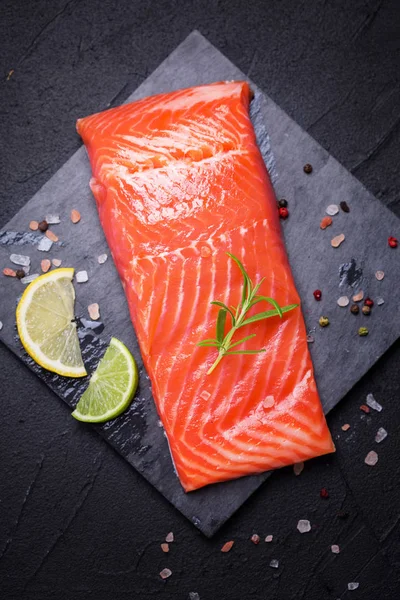 Fresh salmon or trout steak on slate board on black textured bac — Stock Photo, Image