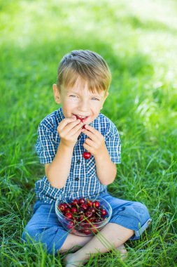 Kiraz plakalı yeşil çimenlerin üzerinde oturan sevimli küçük boy gülümseyerek.