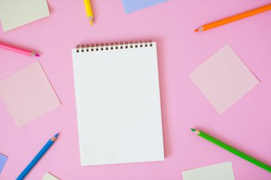 Renkli not kağıtları ve pembe arka plan üzerinde kalemler ile defter.