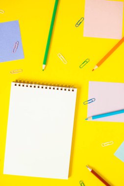 Renkli not kağıtları, klipler ve sarı arka plan üzerinde kalemler ile defter.