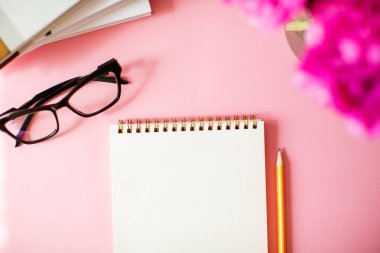Pembe arka plan üzerinde kalem ve gözlüklü defter.