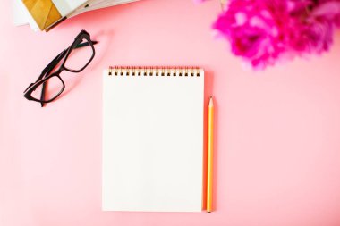 Pembe arka plan üzerinde kalem ve gözlüklü defter.