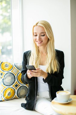 Akıllı telefon ile şehir kafede oturan çekici genç kadın.