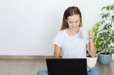 Evde bilgisayar kullanarak çalışan mutlu genç bir kadın. Mesafe öğrenme ve çalışma.