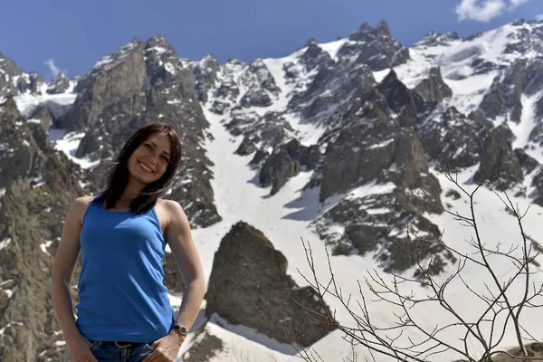 Young woman in t-shirt among snowy mountain peaks.