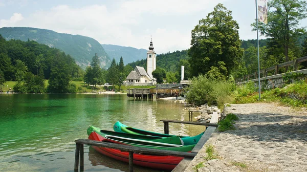 Pintoresca vista de la Iglesia de San Juan Bautista, Alpes Julianos y barcos cerca del lago, Bohinj, Eslovenia — Foto de Stock