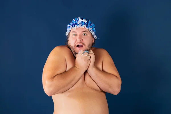 Funny fat man in blue cap and with sponge in the shower. Fun and cleanliness