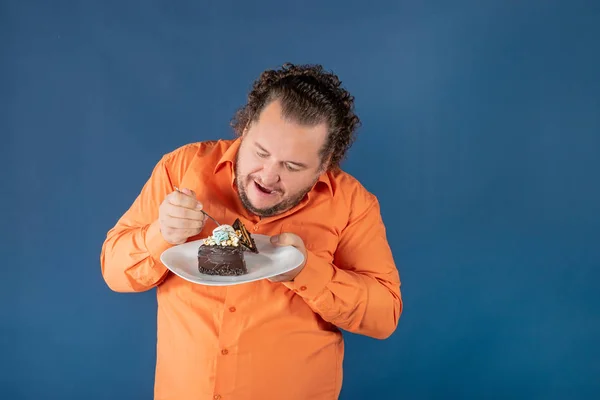 stock image Funny fat man in orange shirt with a piece of chocolate cake on a plate. Birthday celebration