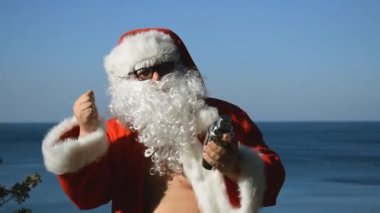 Bir adam Noel Baba kostümlü kokteyl shaker ile sahil üzerinde dans ediyor. Seyahat ve tatil