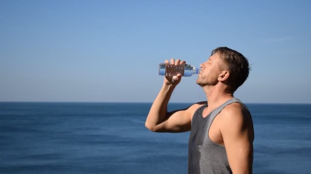 一个男人从海洋上的塑料瓶子里向他的脸上泼水 锻炼后提神 — 图库视频影像